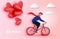 Young riding bicycle and holding red heart paper cut balloons. Love romantic card concept. Happy Valentine`s Day