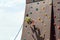 A young rock climber descends from an artificial mountain with safety cords and ropes in a sports amusement park