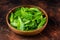 Young romain green salad leaves in wooden plate. Dark background. Top view