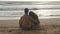 Young romantic couple is enjoying beautiful view sitting on the beach and hugging. A woman and a man sits together in