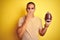 Young rugby player man holding a football ball over yellow isolated background cover mouth with hand shocked with shame for