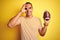 Young rugby player man holding a football ball over yellow isolated background with happy face smiling doing ok sign with hand on