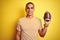 Young rugby player man holding a football ball over yellow isolated background with a happy face standing and smiling with a