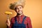 Young rural farmer man holding countryside corn over isolated yellow background with a happy face standing and smiling with a