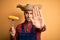 Young rural farmer man holding countryside corn over isolated yellow background with open hand doing stop sign with serious and