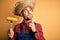 Young rural farmer man holding countryside corn over isolated yellow background serious face thinking about question, very