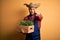 Young rural farmer man wearing countryside hat holding green organic plant from harvest pointing with finger to the camera and to