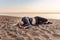 Young sad abandoned woman lies on a sandy beach with a sunset on the background