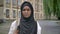 Young sad african muslim woman in hijab looking at camera and standing in park near university, stressed and depressed