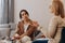 Young sad woman is sitting on the couch, holding her hands to her face at a psychotherapist\'s appointment