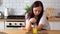 Young sad woman twisting straw in glass of juice, sitting at table in kitchen.