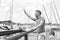 Young sailor waving up on pier with big smile. Yachtsman gives the command by hand to moor in dock. Man welcomes new boat in