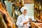 Young salesgirl in white uniform cutting jerky ham for sale in butcher shop