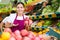 Young saleswoman proposing pomegranate, offering fruits in supermarket