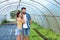 Young satisfied family couple standing in the greenhouse and smiling looking at the vegetables they planted as small business and