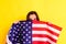 Young scared latin woman covers herself with an american flag in fear of deportations,  on yellow background