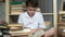 Young schoolboy sits on the floor among the piles of books and reads a textbook