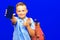 Young schoolboy wears blue t shirt holds phone striped red backpack isolated on blue background