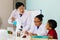 Young scientist holding a flask and teaching two African American mixed kids in chemistry lab