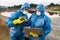 Young scientist in protective coveralls giving stone to colleague with laptop