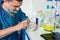 Young scientist in uniform wearing a mask preparing powder on ce