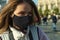 Young self-confident woman wearing black protective mask and walking round the city caring yourself from a virus.