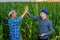 young and senior farmer makes the mark high five in a field of corn.