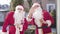 Young and senior Santas standing outdoors and waving at camera. Portrait of two cheerful Santa Clauses wishing merry