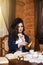 Young Sensual Caucasian Brunette Woman Posing in Retro Style Dress With Coffeepot and Jam Reading Book At The Table in Village