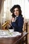 Young Sensual Caucasian Brunette Woman Posing in Retro Style Dress With Coffeepot and Jam At The Table in Village Environment