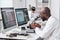 Young serious African man with microscope sitting by workplace