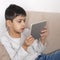 Young serious boy  sitting on the sofa  at home and  using a  tablet for games, communication and for learning