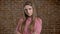 Young serious confident girl with arms crossed, watching at camera, brick background.