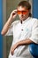 Young serious dentist doctor man in white traditional uniform and glasses standing in dental office in clinic