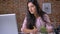 Young serious girl working in a loft office on a laptop, typing, writing a note in a notebook, a brick wall in the