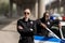 young serious policewoman standing with crossed arms while her partner standing near car and smiling blurred