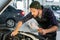 Young serious repairman in workwear holding lamp and bending over open hood