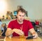 Young serious thoughtful pensive attentive man tense thinking send message by smart phone in red shirt in cafe drinking