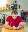 Young serious thoughtful pensive attentive man tense thinking send message by smart phone in red shirt in cafe drinking