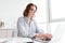 Young serious woman in striped shirt typing email to her boss while sitting at workplace in light apartment