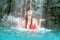 Young sexy blond woman in fuchsia bikini raises her hands against the splashing water of the waterfall