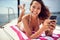 A young sexy girl is posing for a photo while using a smartphone and enjoying a sunbath. Summer, sea, vacation