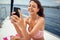 A young sexy girl who is sitting on the towel and chatting on a smartphone while enjoying a sunbath on a yacht. Summer, sea,