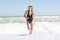 Young sexy woman in black swimsuit and straw hat sunbathes and relaxes on the beach.The girl runs on the waves.