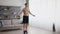 Young shirtless athlete with muscular torso exercising with jumping rope at home, tracking shot, slow motion