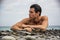 Young shirtless athletic man laying down on pebbles