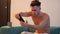 Young shirtless man playinig videogame on smartphone at home