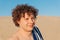 Young shirtless topless Caucasian man with curly hair with striped towel on sandy beach sand dune. Closeup summer headshot