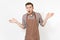 Young shocked bewildered man chef or waiter in striped brown apron, shirt spreading hands isolated on white background