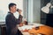 A young shoemaker guy has taken a break from work and is drinking from a paper cup next to a work table with tools and